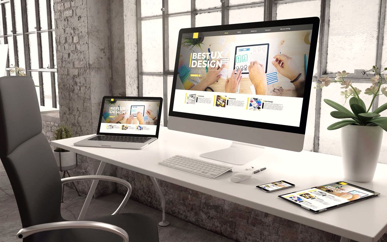 Heller Loft-Arbeitsplatz mit Monitor, Laptop, Tablet und Smartphone, die eine responsive Website zeigen