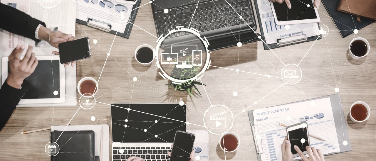 Draufsicht auf einen Besprechungstisch mit Laptops und Tablets, überlagert von einem Netz aus Verbindungen