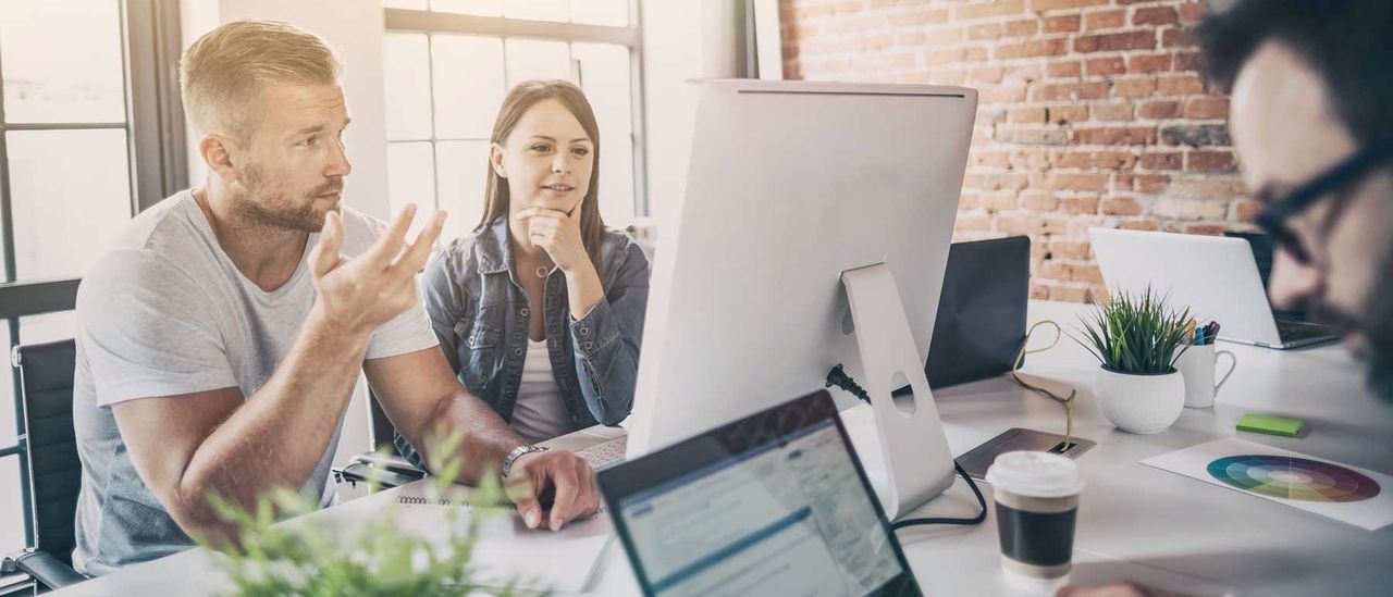 Drei Personen im Gespräch an einem Arbeitstisch in einem Loft-Büro