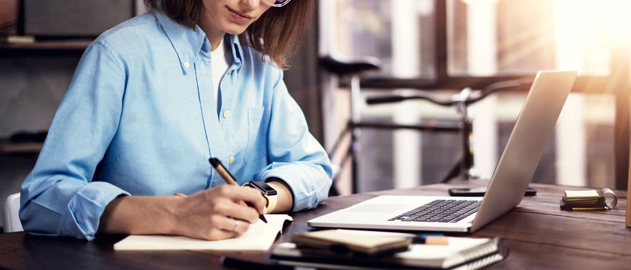 Frau schreibt Notizen am Schreibtisch neben ihrem Laptop