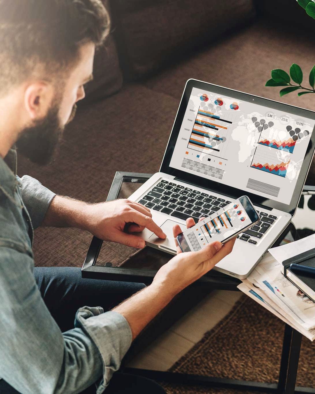 Mann wertet auf Laptop und Smartphone Diagramme aus