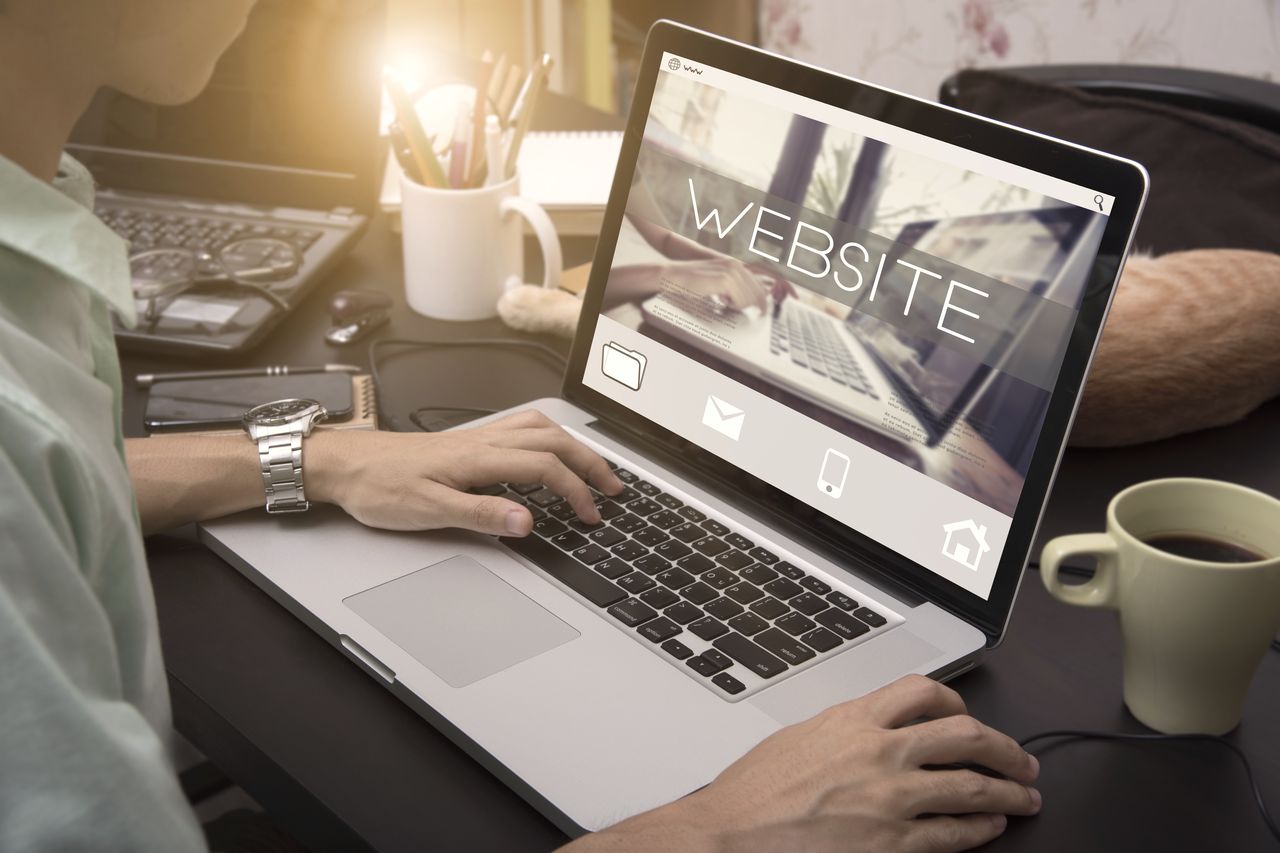 Person arbeitet am Laptop an einer Website, daneben eine Kaffeetasse