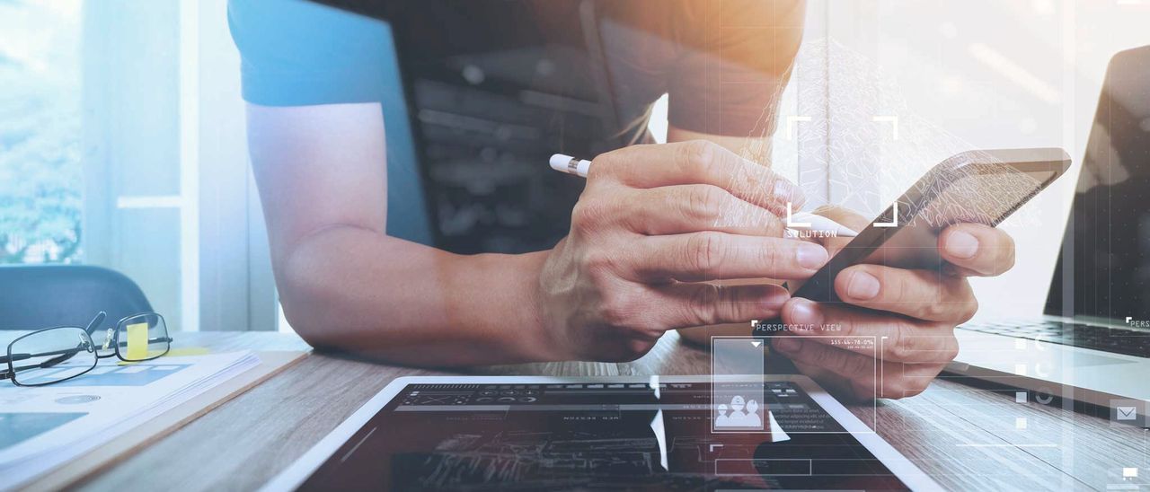 Hände halten ein Smartphone über einem Tablet – eine Website wird auf mobilen Geräten geprüft