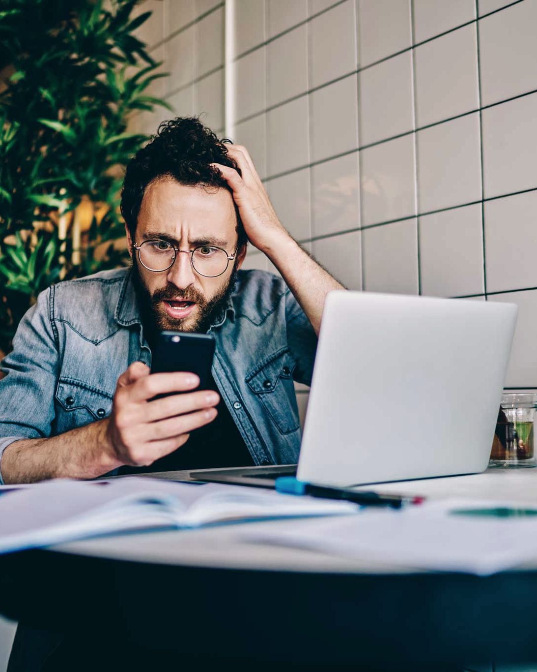 Ratloser Mann blickt am Schreibtisch auf sein Smartphone